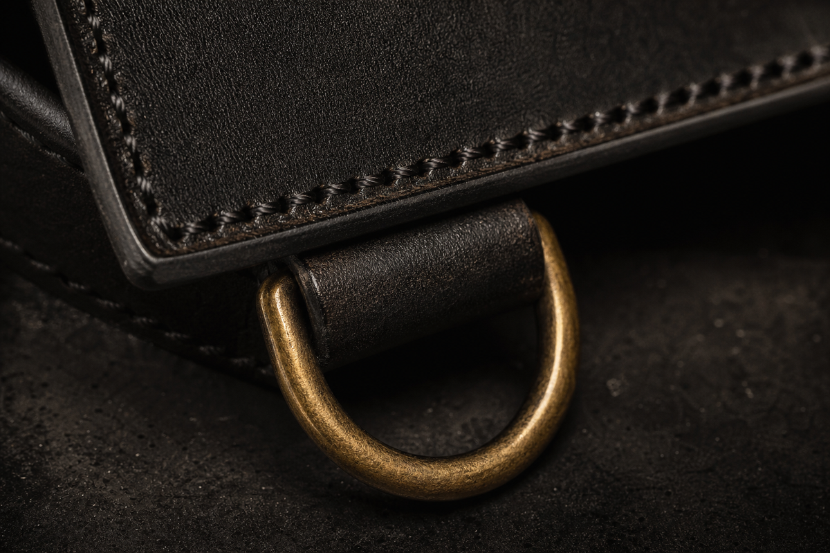 Burnished brass D-ring closure and leather edge on the Brazen Vault Crossbody. Interim render — pending real photography.